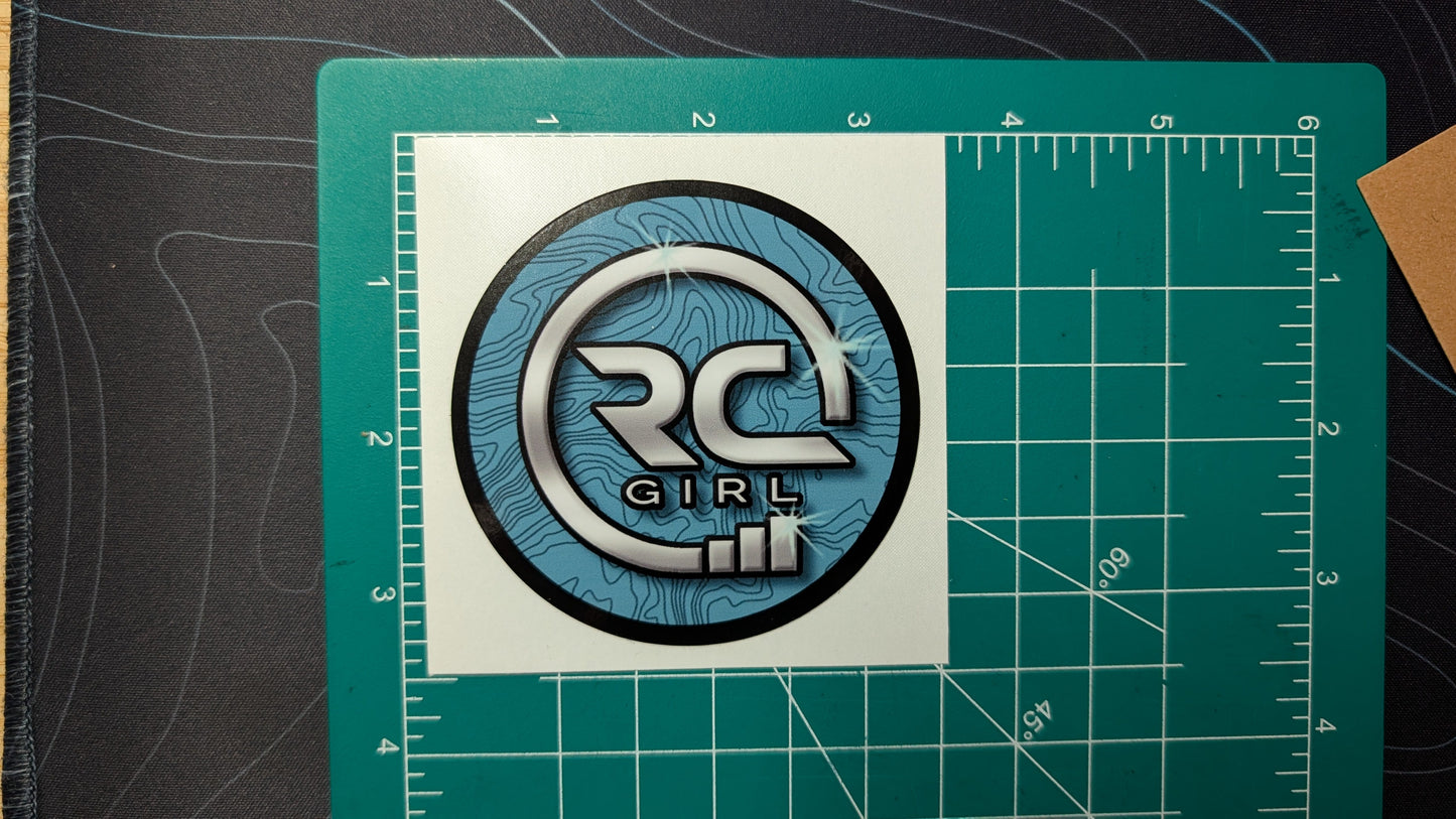 Circular logo with text on a white square, placed on a green cutting mat with measurements.