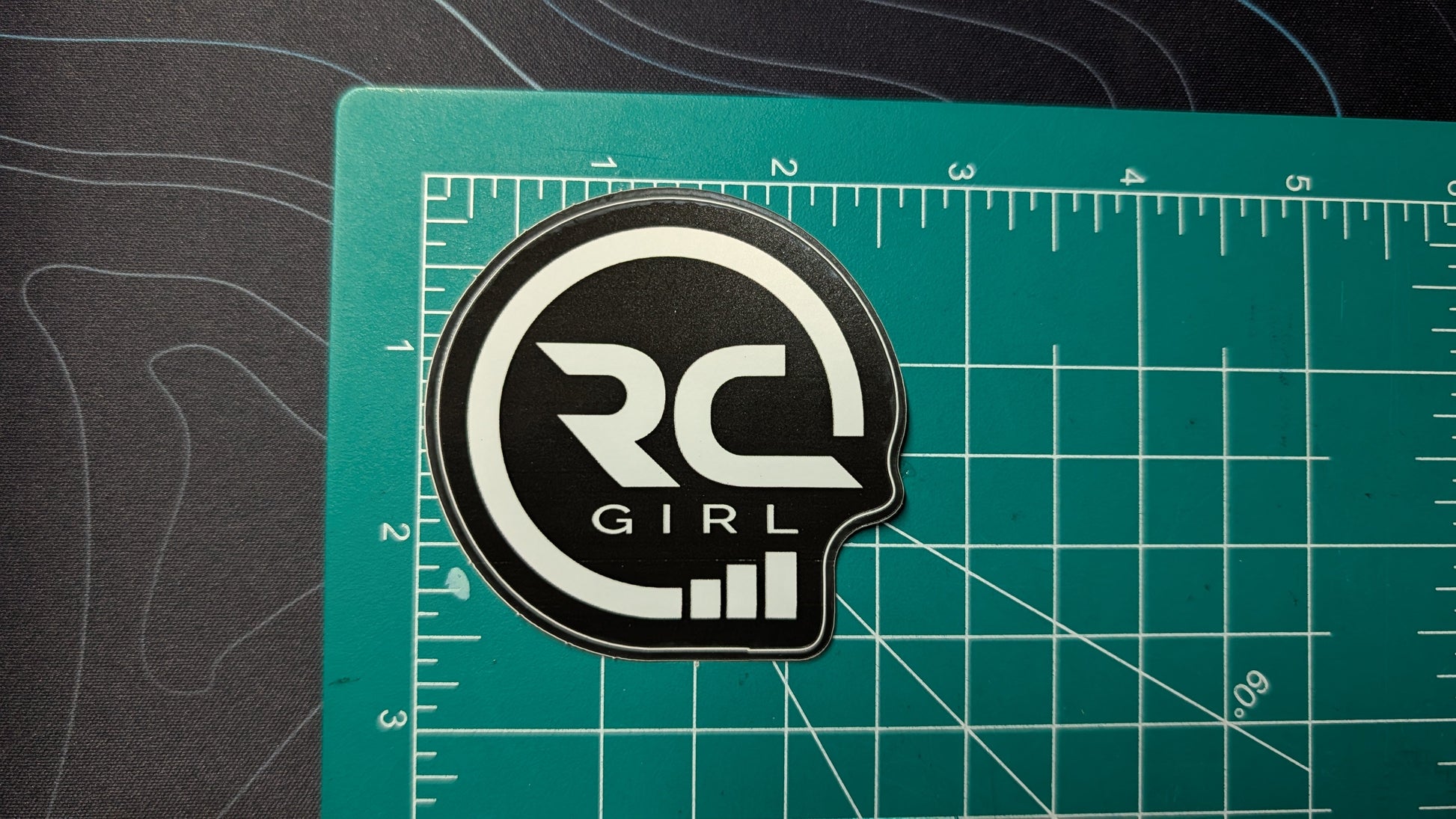 Black and white logo patch on a green cutting mat with ruler